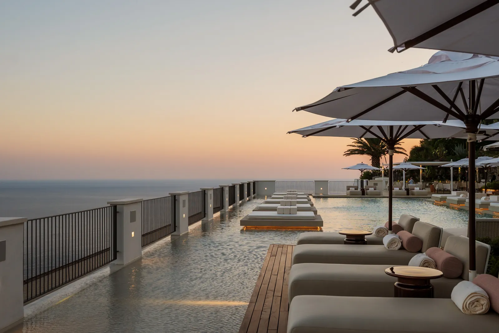 Infinity pool with daybeds and parasols at Furore Grand Hotel at dusk